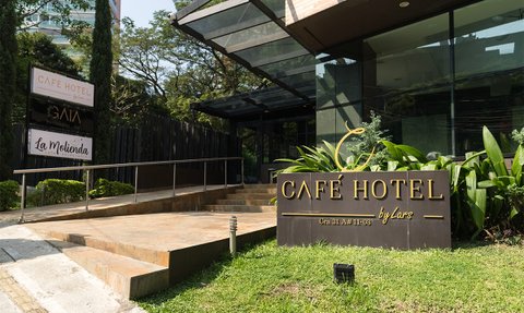Der Eingangsbereich des Café Hotels in Medellín zeigt eine moderne Architektur mit einer einladenden Treppe und Pflanzen.
