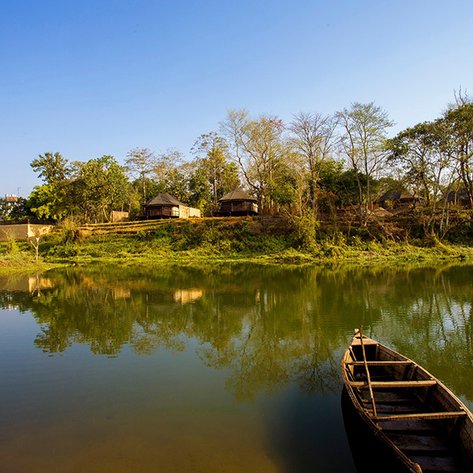 Ein ruhiger Fluss spiegelt die sanfte Landschaft wider, während eine kleine Holzboot am Ufer liegt.