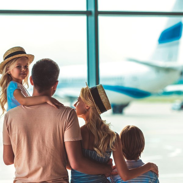 Eine Familie steht am Flughafen und beobachtet ein Flugzeug, während das kleine Mädchen auf dem Arm des Vaters sitzt.