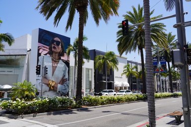 Eine elegante Werbetafel von Saint Laurent zeigt ein Model mit Sonnenbrille und auffälligem Schmuck in einer sonnigen Straße.