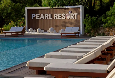 Ein einladender Poolbereich im Pearl Resort, umgeben von Liegen und einer stilvollen Wand mit dem Resort-Namen.