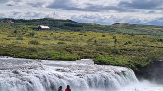 Zwei Mädchen sitzen am Ufer eines rauschenden Wasserfalls und genießen die atemberaubende Landschaft im Hintergrund.