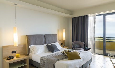 Ein modernes Hotelzimmer mit einem großen Bett, eleganten Lampen und einem Balkon mit Meerblick.