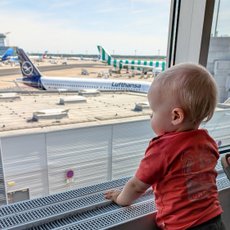 Ein kleines Kind steht am Fenster eines Flughafens und beobachtet die Flugzeuge auf dem Rollfeld mit Neugier.