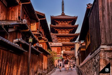 Eine belebte Straße in Kyoto, gesäumt von traditionellen Holzhäusern, führt zur beeindruckenden Pagode im Hintergrund.