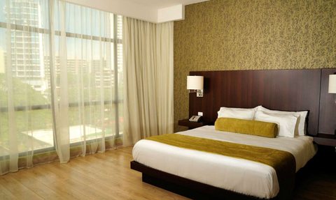 Ein modernes Hotelzimmer mit einem großen Bett, das mit weißen und gelben Kissen dekoriert ist, und einem eleganten Holzboden.