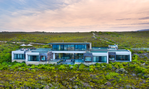 Ein modernes, elegantes Haus mit großen Fenstern steht inmitten einer üppigen, grünen Landschaft unter einem sanften Himmel.