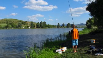 Ein Angler steht am Ufer eines ruhigen Sees, während er seine Angelrute in die Ferne hält und die Natur genießt.