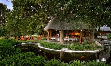 Ein einladendes Restaurant mit Strohdach, umgeben von üppigem Grün und einem ruhigen Teich, der die Natur widerspiegelt.