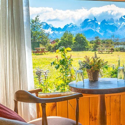 Ein gemütlicher Raum mit Holzverkleidung, Blick auf die majestätischen Berge und eine grüne Wiese durch ein großes Fenster.