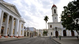 Eine ruhige Straße in Cienfuegos, gesäumt von historischen Gebäuden und einer Kirche mit einem markanten Glockenturm.