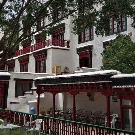 Ein traditionelles Hotelgebäude mit weißen Wänden und roten Akzenten, umgeben von Bäumen und einem einladenden Garten.