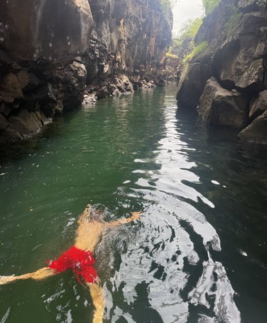 Ein Junge schwimmt entspannt in einem ruhigen, grünen Wasser zwischen hohen, steilen Felsen.
