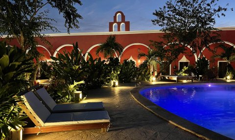 Ein ruhiger Poolbereich mit blauen Wasser und bequemen Liegen, umgeben von üppigem Grün und sanfter Beleuchtung in der Dämmerung.