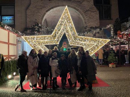 Eine Gruppe von Frauen posiert fröhlich vor einem großen, leuchtenden Weihnachtsstern auf einem festlichen Markt.
