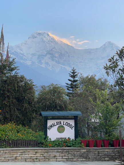 Der Himalaya Lodge-Schild steht vor einer beeindruckenden Berglandschaft mit schneebedeckten Gipfeln im Hintergrund.