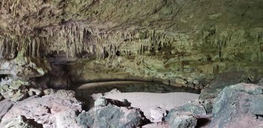 Eine beeindruckende Höhle mit tropfenden Stalaktiten und einer sandigen Fläche, die von Felsen umgeben ist.
