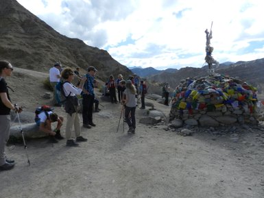 Eine Gruppe von Wanderern pausiert in einer bergigen Landschaft, umgeben von bunten Gebetsfahnen und einem Steinhaufen.