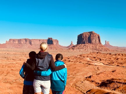 Drei Personen stehen mit dem Rücken zur Kamera und betrachten die beeindruckenden Felsformationen von Monument Valley.