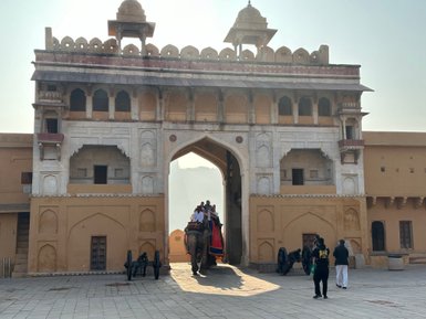 Ein majestätisches Tor des Amber Fort in Jaipur, durch das ein Elefant mit Passagieren schreitet, umgeben von historischen Gebäuden.