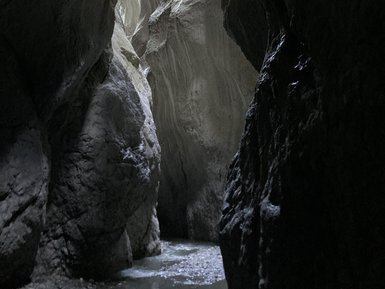 Ein schmaler, dunkler Canyon mit hohen, gewundenen Felswänden, durch den ein schmaler Wasserlauf fließt.