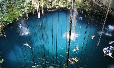 Personen schwimmen im klaren Wasser eines unterirdischen Cenote mit Lichtöffnung – Mexiko mit Kindern