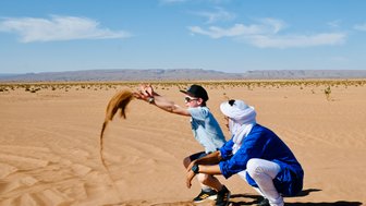 Guide und Kind spielen gemeinsam und werfen Sand in der weiten Wüste – Familienreise nach Marokko