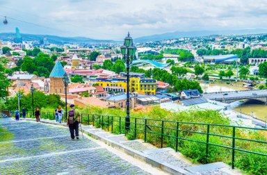 Ein malerischer Blick auf Tiflis mit bunten Gebäuden und einer Seilbahn, die über die Stadt schwebt.