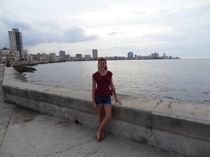 Eine Frau steht am Ufer, lächelt und genießt die Aussicht auf das Wasser und die Stadt im Hintergrund.
