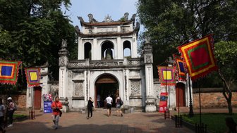 Der Eingang zum Literaturtempel in Hanoi, umgeben von bunten Fahnen und Besuchern, die die historische Stätte erkunden.