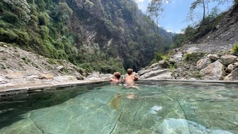 Zwei Personen entspannen in einem heißen Quellbecken, umgeben von einer beeindruckenden Berglandschaft in Nepal.