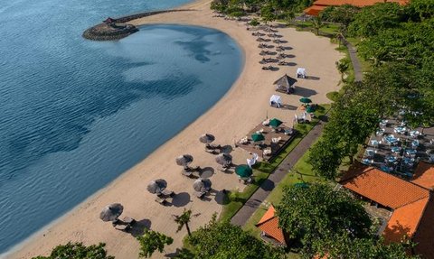Ein malerischer Strand mit Sonnenliegen und Sonnenschirmen, umgeben von üppigem Grün und klarem Wasser.