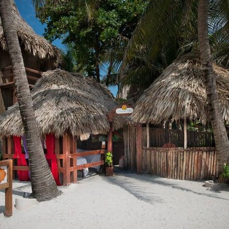 Ein einladendes Restaurant mit Strohdach, umgeben von Palmen und weißem Sand, strahlt tropisches Flair aus.