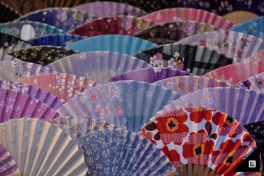 Eine Vielzahl von bunten Fächern in verschiedenen Designs und Farben, die übereinander angeordnet sind und ein lebhaftes Bild erzeugen.