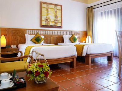 Ein helles Zimmer mit zwei Betten, dekoriert mit gelben Kissen und einer warmen Atmosphäre durch sanftes Licht.