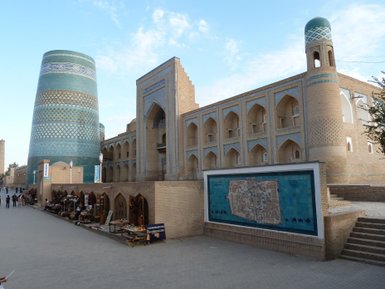 Eine belebte Straße mit traditionellen Ständen, umgeben von beeindruckender Architektur und einem blauen Himmel.