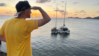 Ein Mann in einem gelben T-Shirt schaut in die Ferne, während die Sonne über dem Wasser untergeht.