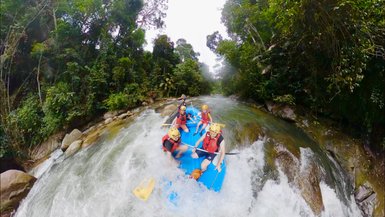 Familie sitzt gemeinsam in einem Schlauchboot und paddelt durch den Fluss – Malaysia & Borneo Reise mit Kindern