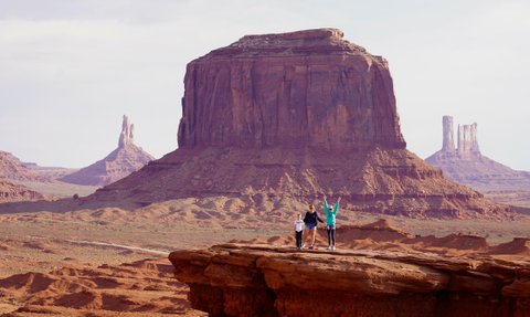 Drei Personen stehen auf einer Felsplattform in Monument Valley, umgeben von beeindruckenden roten Felsen und Hügeln.