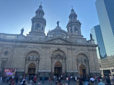 Die beeindruckende Fassade einer Kathedrale mit zwei Türmen und Statuen, umgeben von Menschen und modernen Gebäuden.