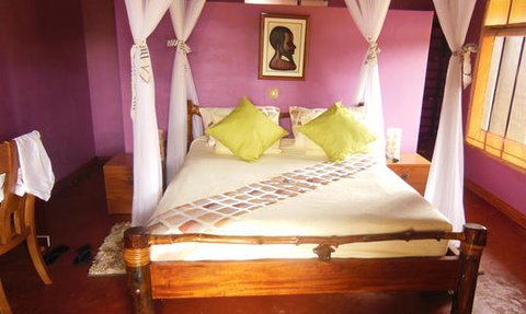 Ein gemütliches Schlafzimmer mit einem großen Bett, umgeben von weißen Moskitonetzen und lila Wänden, strahlt Ruhe aus.