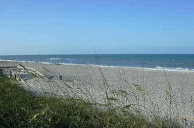 Ein ruhiger Strand mit feinem Sand erstreckt sich unter einem klaren blauen Himmel, während sanfte Wellen ans Ufer rollen.