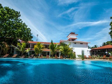 Ein luxuriöses Hotel am Strand mit einem glitzernden Pool, umgeben von üppigem Grün und sonnigem Himmel.