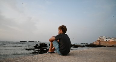 Kind sitzt ruhig im Sand am Strand von Essaouira und schaut auf das Meer – Marokko mit Kindern