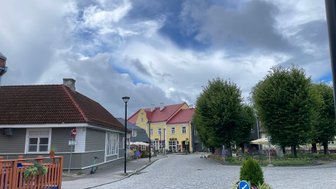 Eine malerische Straßenszene mit bunten Häusern und einem klaren Himmel, umgeben von grünen Bäumen und gepflasterten Wegen.