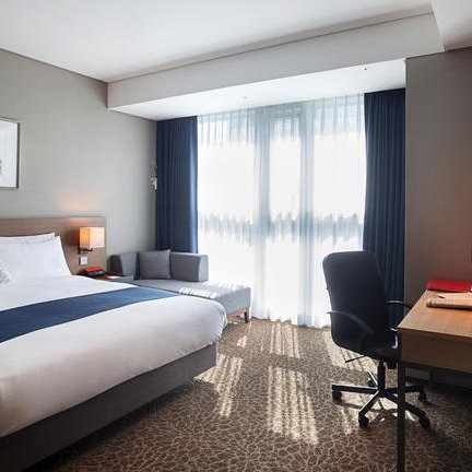 Ein modernes Hotelzimmer mit einem großen Bett, einem Schreibtisch und einem gemütlichen Sitzbereich neben einem Fenster.