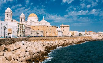 Die Küstenlinie von Cádiz zeigt historische Gebäude und eine beeindruckende Kathedrale vor einem strahlend blauen Himmel.