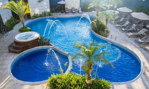 Ein einladender Pool mit kühlen blauen Wasserfontänen, umgeben von grünen Palmen und Sonnenliegen für Entspannung.