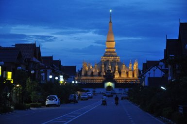 Eine beleuchtete Pagode erhebt sich majestätisch über eine ruhige Straße, umgeben von traditionellen Häusern im Dämmerlicht.