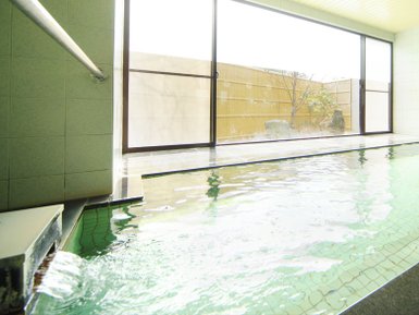 Ein entspannendes Onsen mit klarem Wasser, das sanft plätschert, umgeben von großen Fenstern und einem ruhigen Außenbereich.